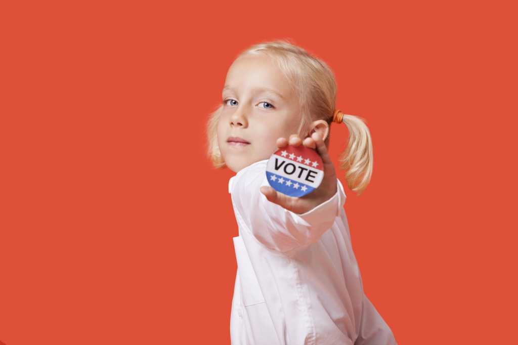 girl with pigtails against orange background holding out vote election pin