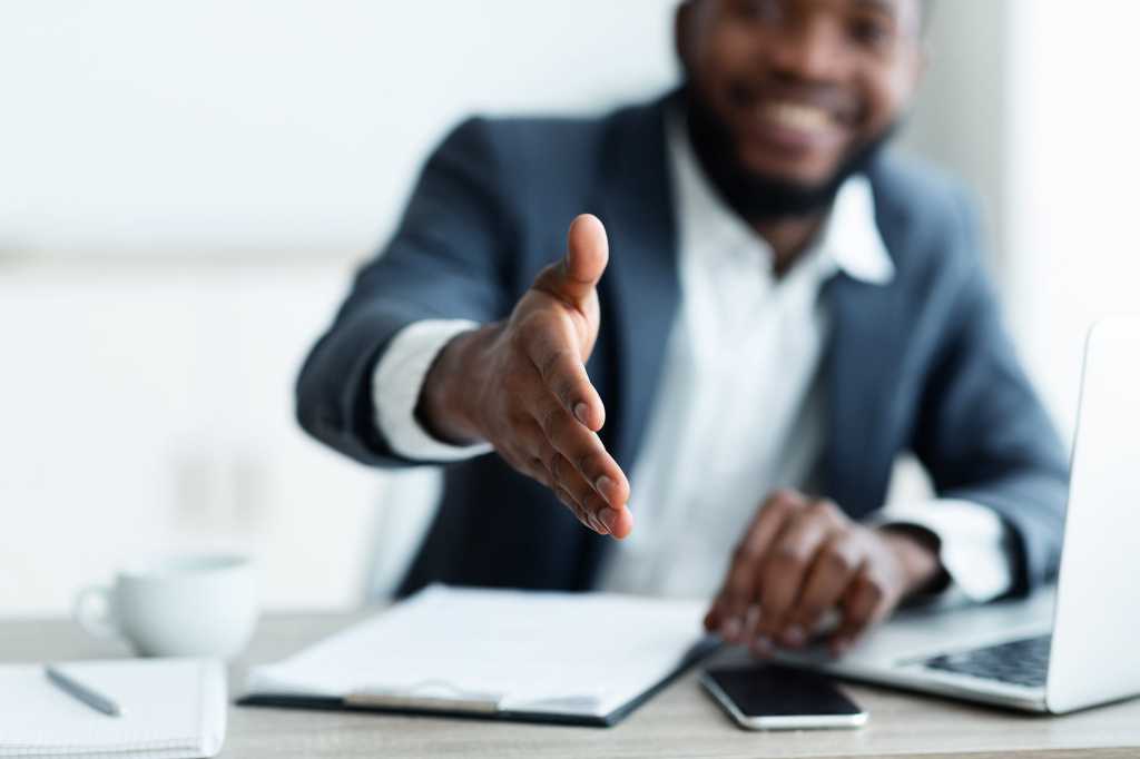 A businessman extends his right arm to shake hands. [handshake / trust / partnership / teamwork]
