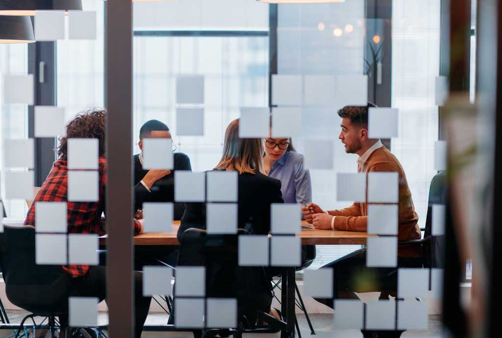 In a sleek glass office space, a team of business professionals engage in lively discussions and exchange strategic ideas, showcasing collaboration and innovation at the heart of modern corporate